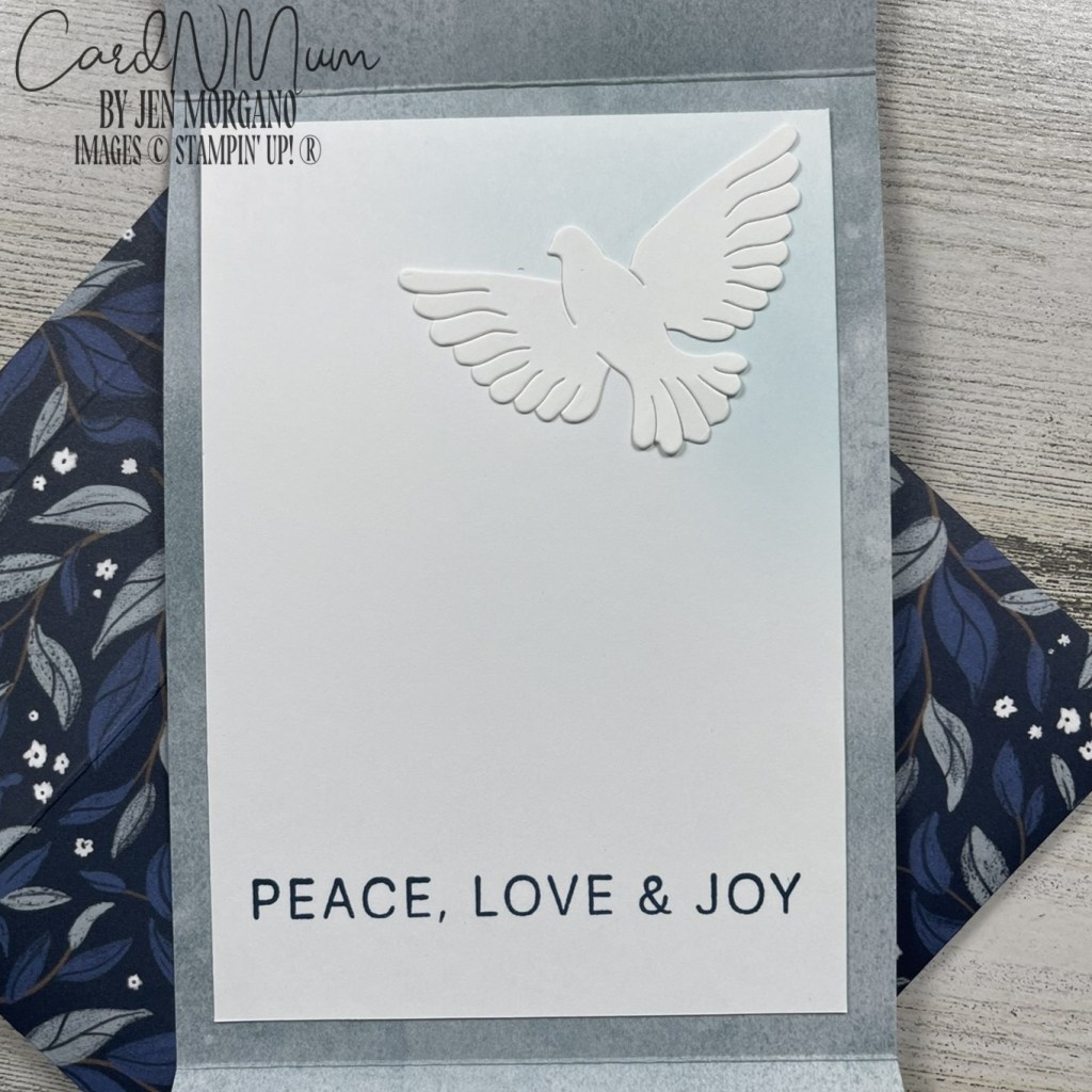 An open greeting card featuring a white dove silhouette and the text 'PEACE, LOVE & JOY' on a pale blue background. The card is surrounded by a floral patterned envelope.