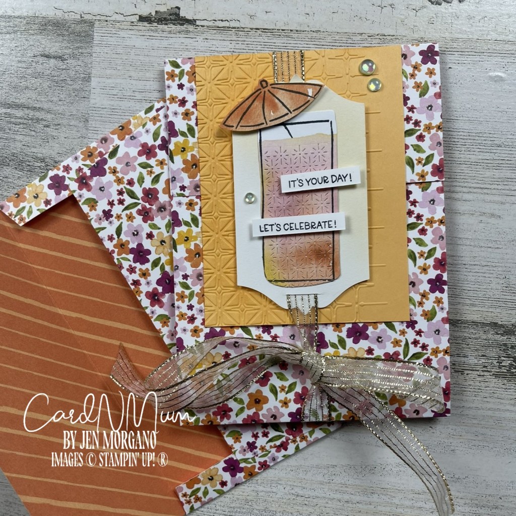 A handmade card featuring a colorful drink illustration, embellishments, and festive phrases 'IT'S YOUR DAY!' and 'LET'S CELEBRATE!' on a textured background, paired with a matching envelope decorated with floral patterns.