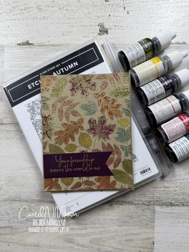 A handmade card featuring a stamped autumn leaf design with gold and colored accents, placed next to a stamp set labeled 'Etched Autumn' and watercolor ink bottles.