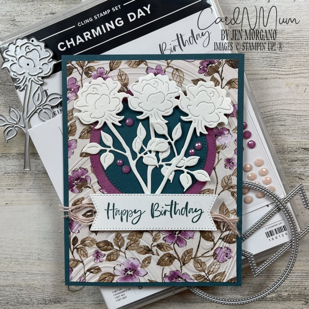 A handmade birthday card featuring layered flowers, a circular background, and the text 'Happy Birthday' on a decorative background with floral patterns.