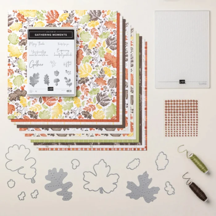 Flat lay featuring the Gathering Moments bundle, including colorful patterned paper, a stamp set with leaf designs, dies in leaf shapes, adhesive dots, and tools for crafting.