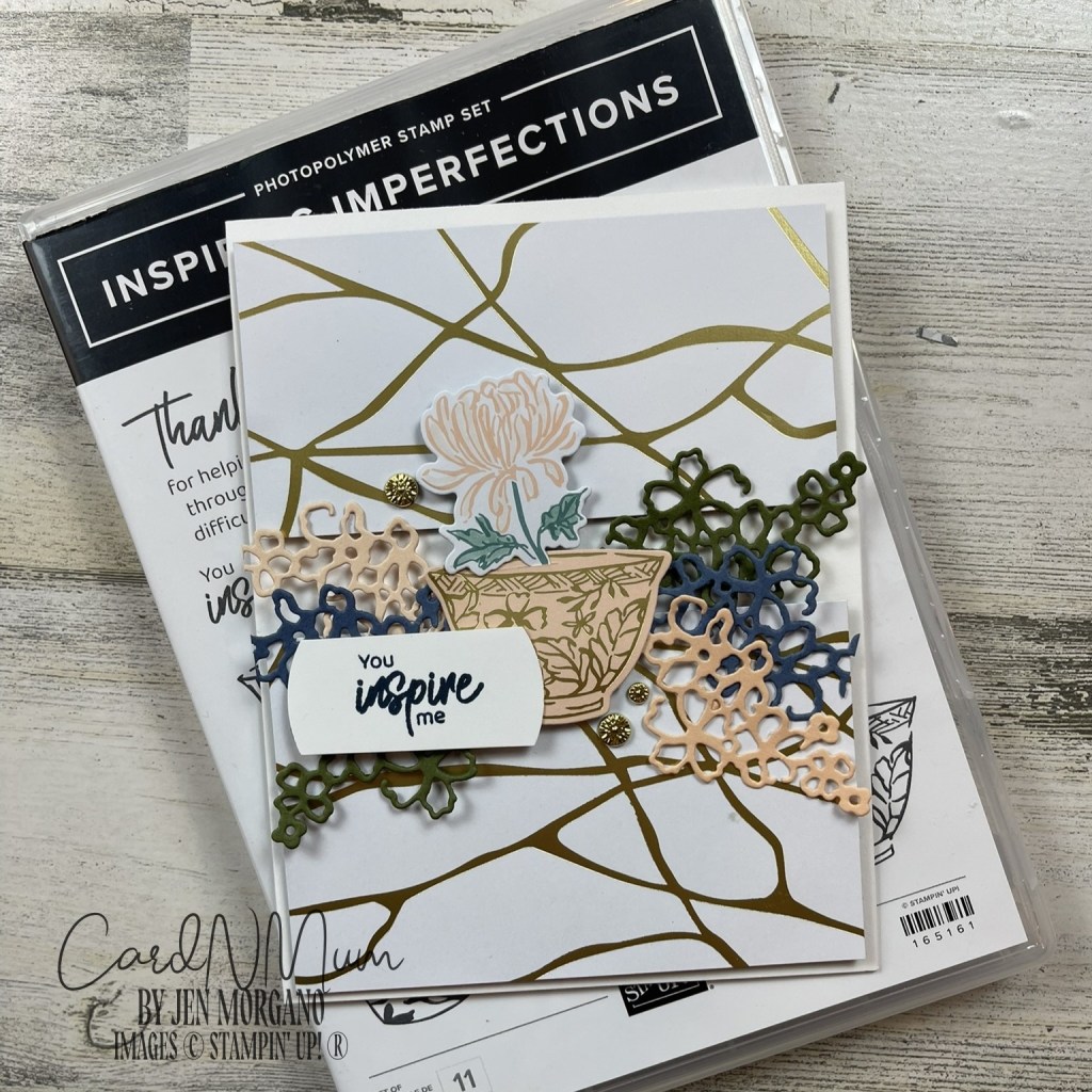 A greeting card featuring a floral design with a potted plant, layered with decorative paper elements and the phrase 'You inspire me'. The card is placed on top of a packaging for a photopolymer stamp set titled 'Inspiring Imperfections'.