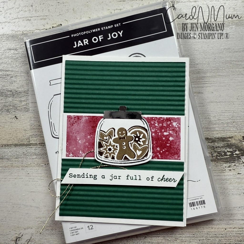 A handmade greeting card featuring a green striped background, an illustration of a jar with a gingerbread man and stars inside, and the text 'Sending a jar full of cheer'.