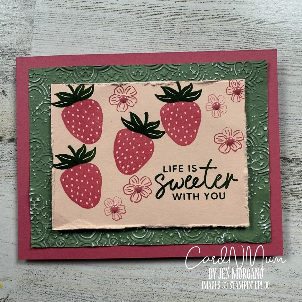 A handmade card featuring a design of several strawberries, flowers, and the phrase 'LIFE IS SWEETER WITH YOU', set against a textured green background and a pink border.
