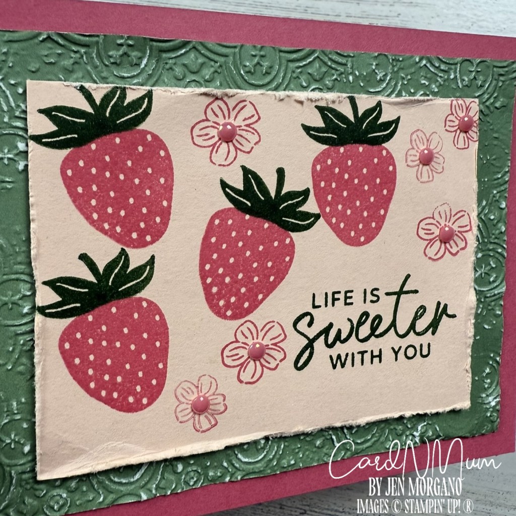 A handmade card featuring stamped strawberries, flowers, and the text 'LIFE IS SWEETER WITH YOU' on a textured green background.