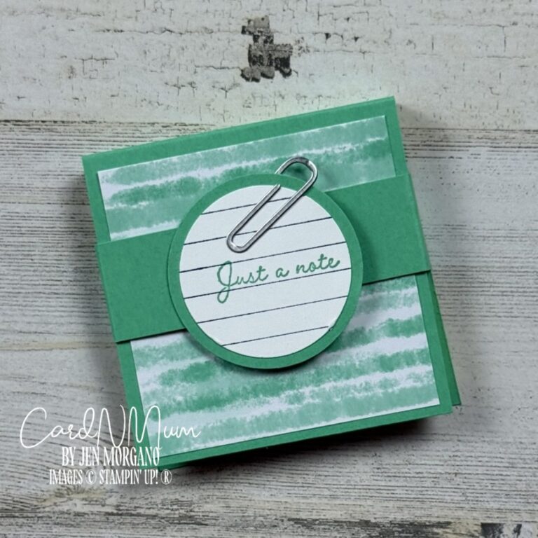 A hand-crafted Post-It Note holder featuring a green and white striped design, with a circular label saying 'Just a note' attached by a silver paperclip.