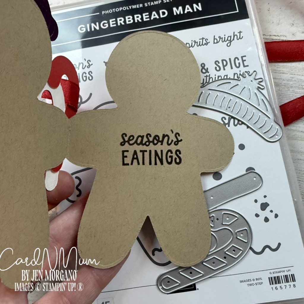 A close-up of a gingerbread man-shaped tag made of kraft paper, featuring the text 'season's eatings' printed on it, with the Stampin' Up! Gingerbread Man stamp set and other crafting elements in the background.