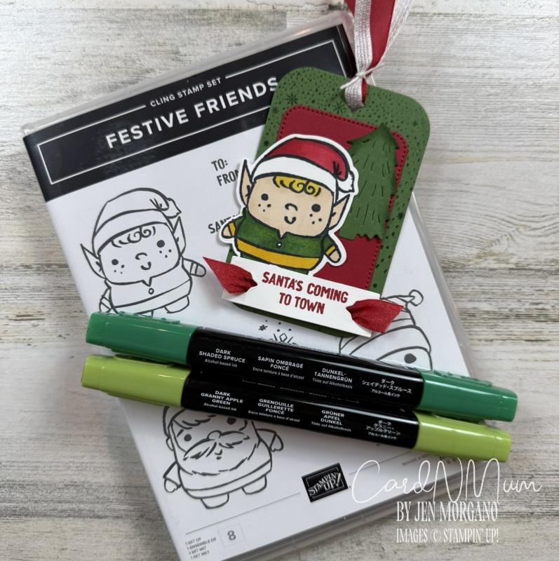 A festive crafting setup featuring a stamp set labeled 'Festive Friends', colorful markers in shades of green, and a tag with the text 'Santa's Coming to Town'.
