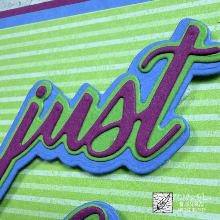 Close-up of a handmade Stampin’ Up! card featuring a layered die-cut “just” sentiment in bright purple, green, and blue cardstock on a striped background.